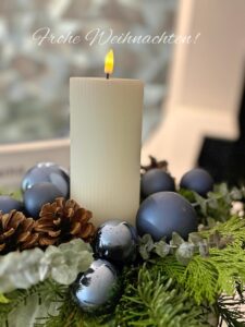 Eine weiße Kerze brennt ruhig in einem Adventskranz mit blauen Kugeln und Tannenzweigen